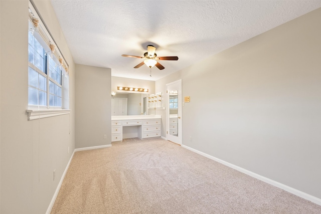 unfurnished bedroom featuring ceiling fan, carpet flooring, built in desk, and a textured ceiling