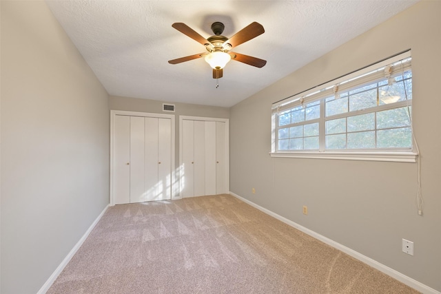 unfurnished bedroom featuring multiple closets, ceiling fan, light carpet, and a textured ceiling