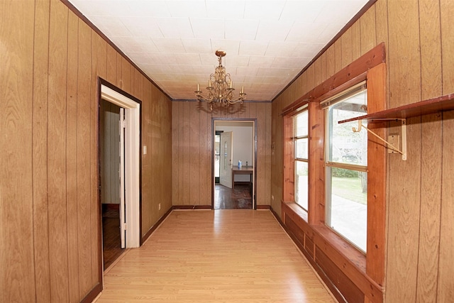 corridor featuring wood walls, crown molding, a notable chandelier, and light hardwood / wood-style flooring