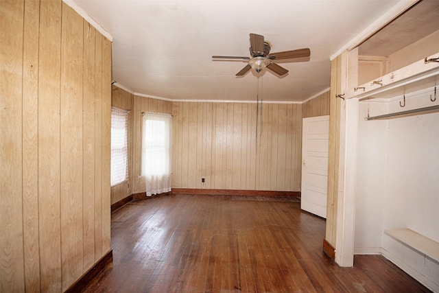 unfurnished room with crown molding, dark hardwood / wood-style floors, ceiling fan, and wood walls