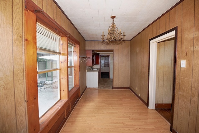 hall with a notable chandelier, ornamental molding, wooden walls, and light wood-type flooring