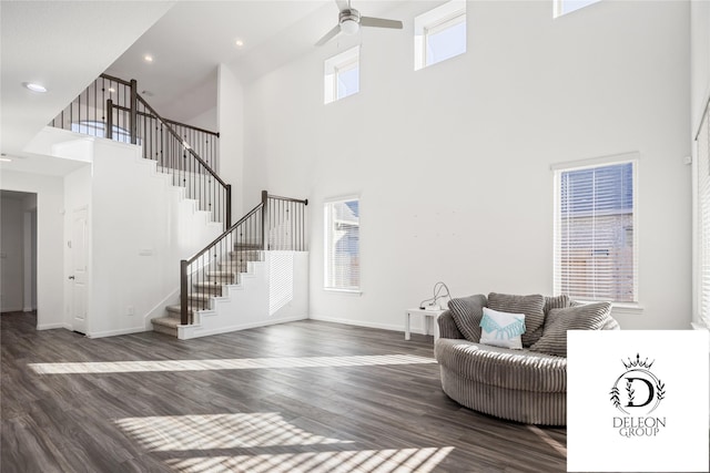 living room with ceiling fan, plenty of natural light, a towering ceiling, and dark hardwood / wood-style flooring