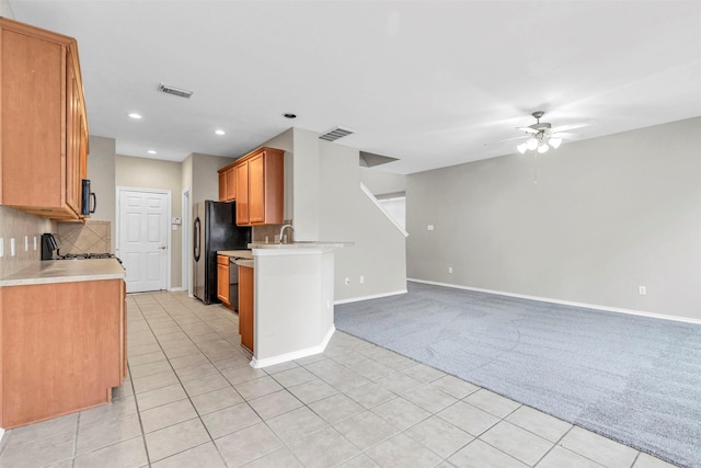 kitchen with black refrigerator, tasteful backsplash, light colored carpet, range, and ceiling fan