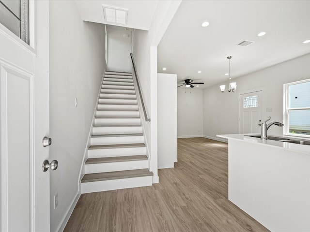 stairway with sink, hardwood / wood-style flooring, and ceiling fan with notable chandelier