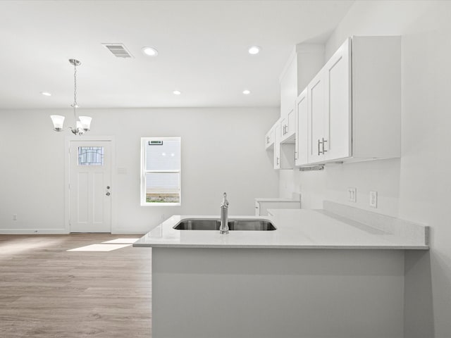 kitchen with sink, white cabinetry, hanging light fixtures, light hardwood / wood-style floors, and kitchen peninsula