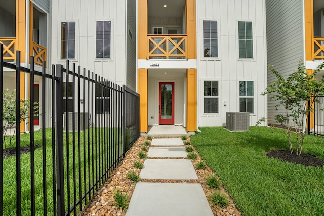 view of exterior entry with board and batten siding, a yard, central AC, and fence