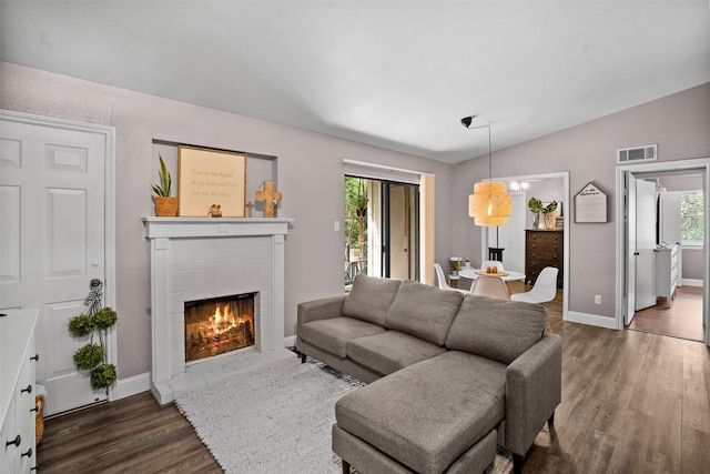 living room with vaulted ceiling, a brick fireplace, and dark wood-type flooring