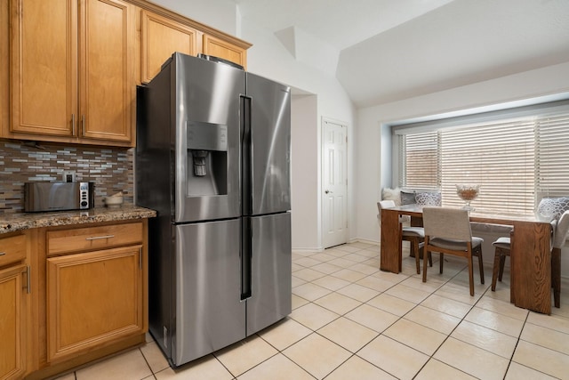 kitchen featuring lofted ceiling, tasteful backsplash, stainless steel fridge with ice dispenser, light tile patterned floors, and dark stone counters