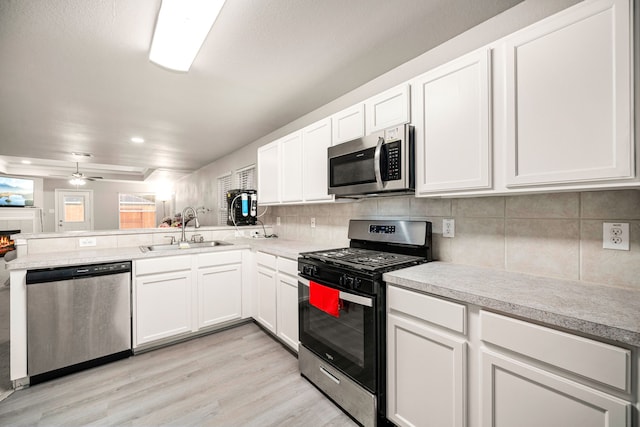 kitchen with sink, white cabinetry, backsplash, stainless steel appliances, and a tiled fireplace