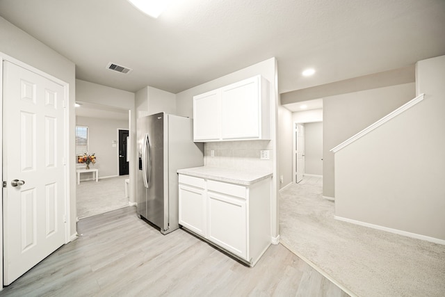 kitchen with stainless steel refrigerator with ice dispenser, white cabinetry, light wood-type flooring, and decorative backsplash