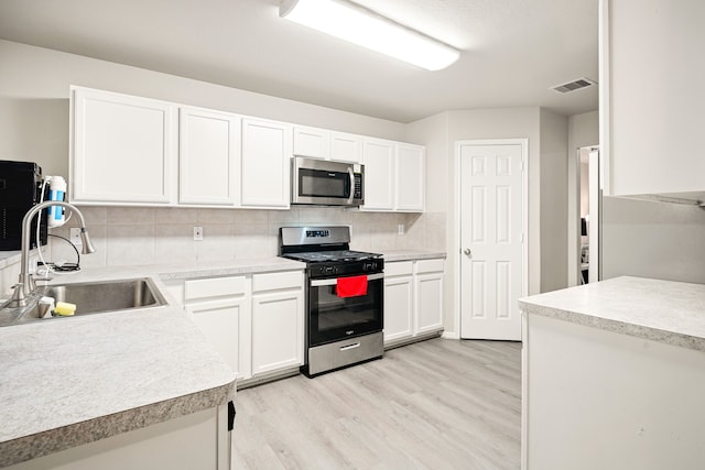 kitchen with sink, white cabinets, decorative backsplash, stainless steel appliances, and light wood-type flooring