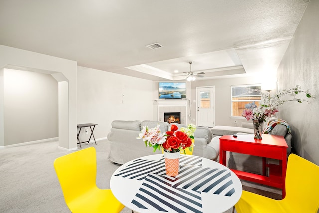 carpeted living room featuring ceiling fan, a fireplace, and a tray ceiling