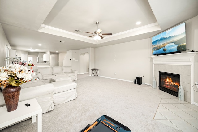 carpeted living room featuring a raised ceiling, ceiling fan, crown molding, and a fireplace