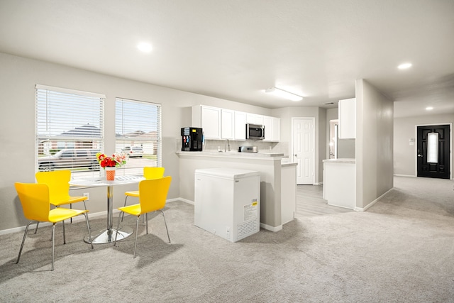 kitchen featuring light colored carpet, white cabinets, backsplash, and kitchen peninsula