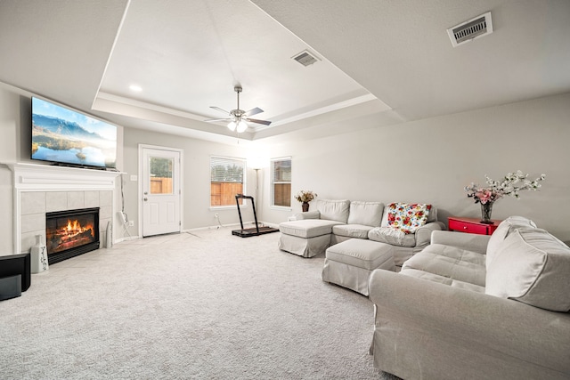 living room with ceiling fan, carpet flooring, a tray ceiling, and a tiled fireplace