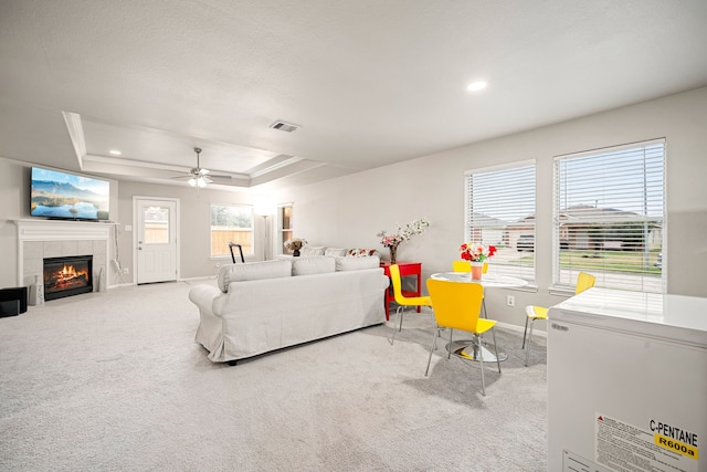 carpeted bedroom featuring a raised ceiling, ceiling fan, a fireplace, and multiple windows