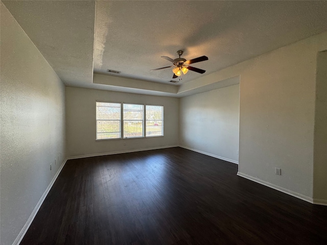 spare room with ceiling fan, dark hardwood / wood-style floors, a raised ceiling, and a textured ceiling