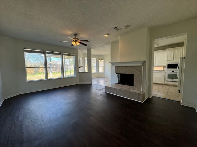 unfurnished living room featuring dark wood-type flooring, ceiling fan, a fireplace, and a textured ceiling