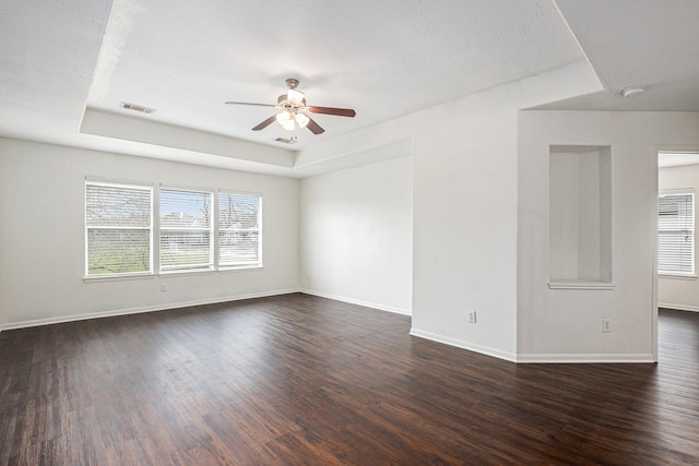 spare room with ceiling fan, dark wood-type flooring, visible vents, baseboards, and a raised ceiling