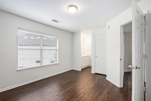 unfurnished bedroom featuring connected bathroom, dark wood finished floors, visible vents, and baseboards