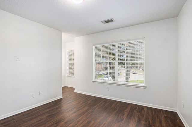 unfurnished room featuring dark wood-style flooring, visible vents, a textured ceiling, and baseboards