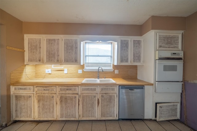 kitchen featuring sink, decorative backsplash, stainless steel dishwasher, white oven, and light brown cabinets