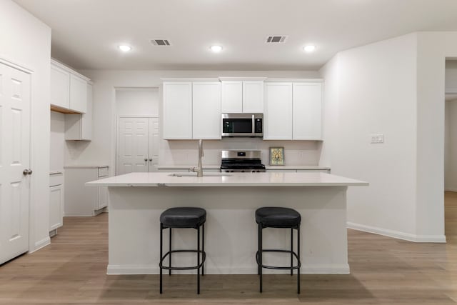 kitchen featuring white cabinetry, sink, a kitchen island with sink, stainless steel appliances, and light hardwood / wood-style flooring