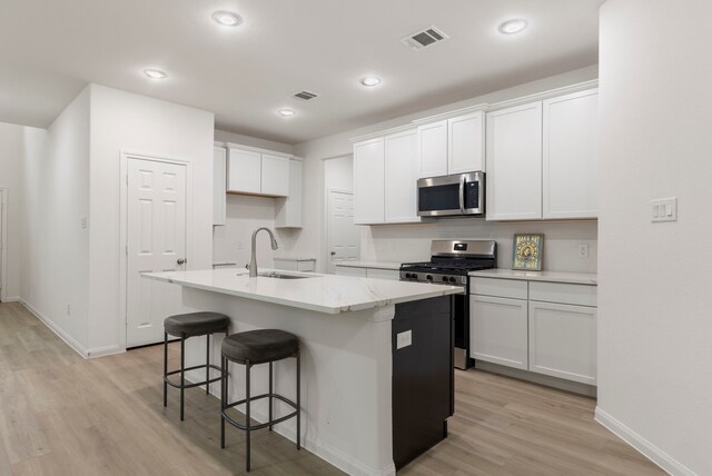 kitchen with sink, white cabinets, a kitchen island with sink, light hardwood / wood-style floors, and stainless steel appliances