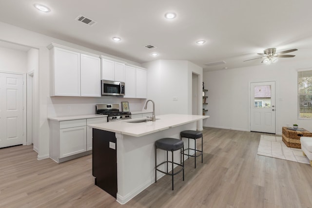 kitchen with sink, light hardwood / wood-style flooring, appliances with stainless steel finishes, an island with sink, and white cabinets