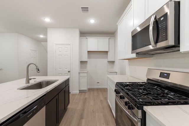 kitchen featuring stainless steel appliances, white cabinetry, light stone countertops, and sink