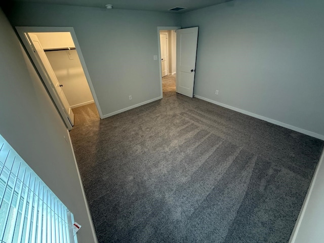 unfurnished bedroom featuring a walk in closet and dark carpet