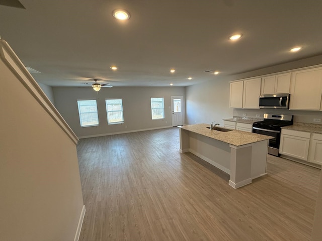 kitchen featuring light wood-type flooring, stainless steel appliances, an island with sink, and white cabinets