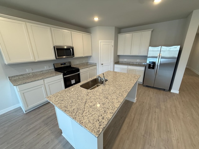 kitchen featuring sink, appliances with stainless steel finishes, light stone counters, an island with sink, and white cabinets