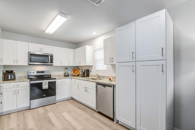 kitchen featuring white cabinetry, sink, light hardwood / wood-style floors, stainless steel appliances, and light stone countertops