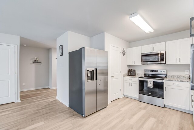 kitchen with stainless steel appliances, white cabinetry, and light stone countertops