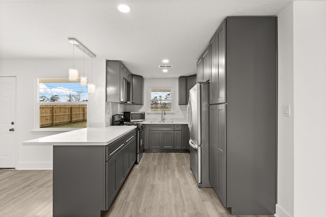 kitchen featuring appliances with stainless steel finishes, pendant lighting, gray cabinetry, kitchen peninsula, and light wood-type flooring