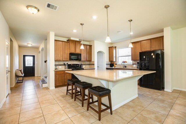 kitchen with pendant lighting, a kitchen breakfast bar, a center island, light stone countertops, and black appliances