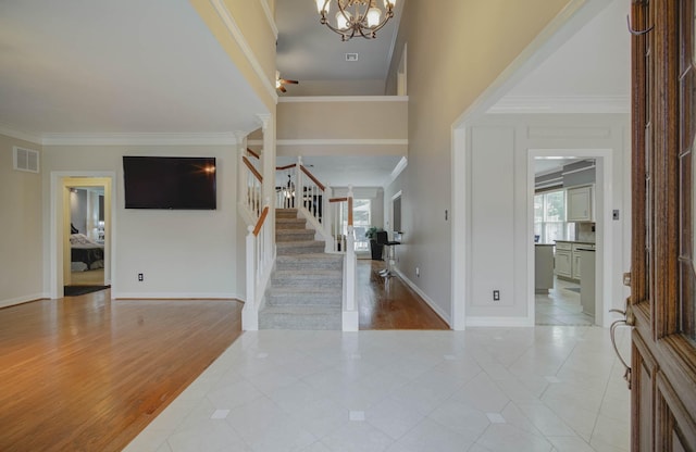 foyer entrance with an inviting chandelier, light tile patterned floors, crown molding, and a high ceiling