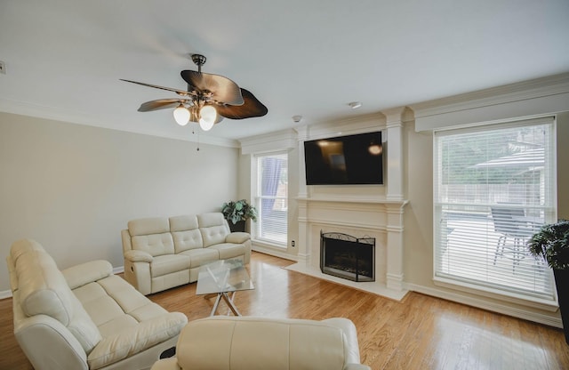 living room with a premium fireplace, ornamental molding, ceiling fan, and light hardwood / wood-style floors