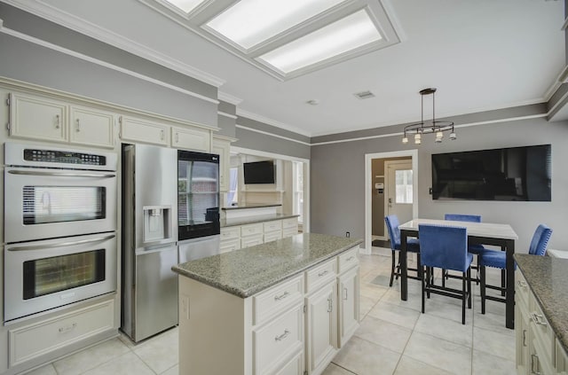 kitchen featuring crown molding, hanging light fixtures, light tile patterned floors, a kitchen island, and stainless steel appliances