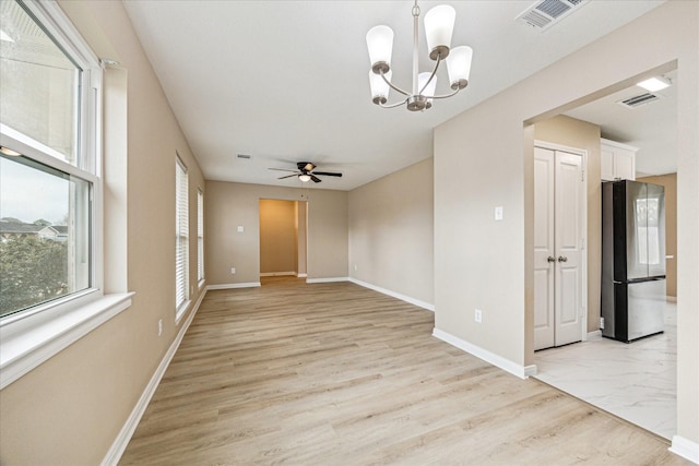 empty room with ceiling fan with notable chandelier and light hardwood / wood-style flooring