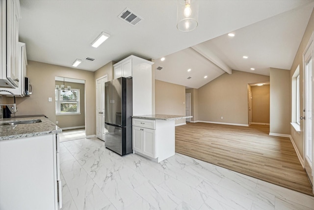 kitchen with sink, light stone counters, white cabinets, and stainless steel refrigerator