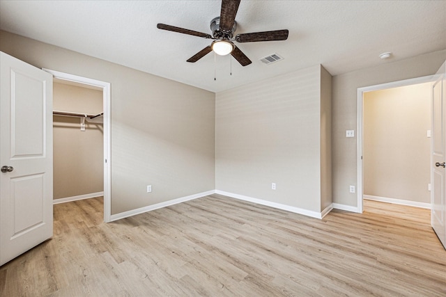 unfurnished bedroom with ceiling fan, a walk in closet, light wood-type flooring, and a closet