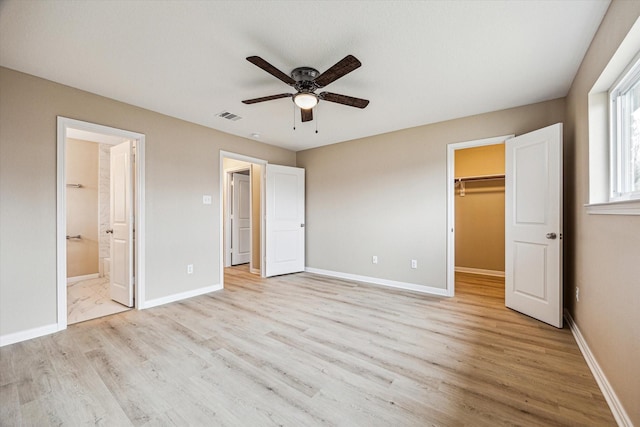 unfurnished bedroom featuring ensuite bathroom, a spacious closet, a closet, ceiling fan, and light hardwood / wood-style floors