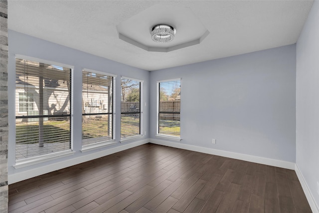 empty room with a tray ceiling, dark wood-type flooring, and a textured ceiling