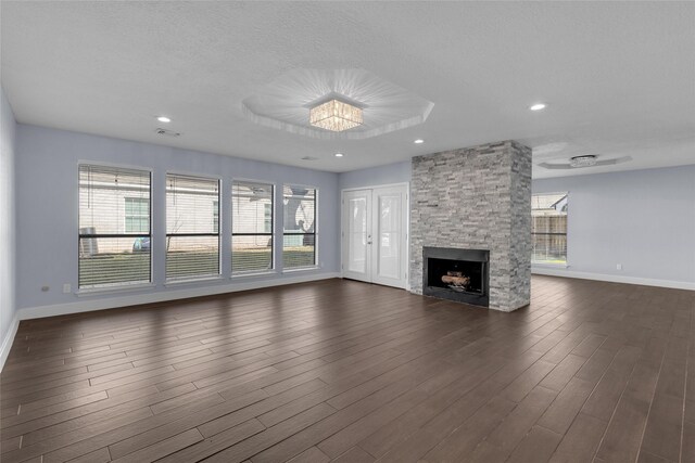 unfurnished living room featuring dark wood-type flooring, a stone fireplace, a textured ceiling, and a wealth of natural light