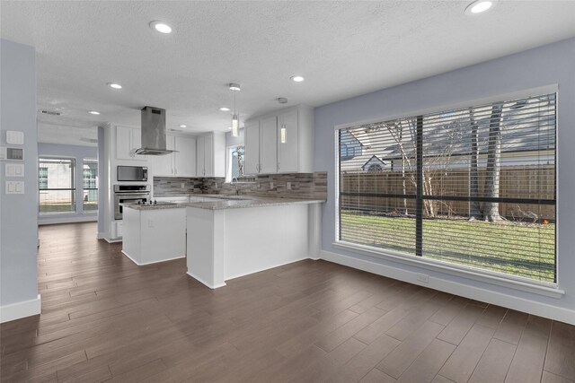 kitchen with island range hood, built in microwave, white cabinetry, oven, and kitchen peninsula