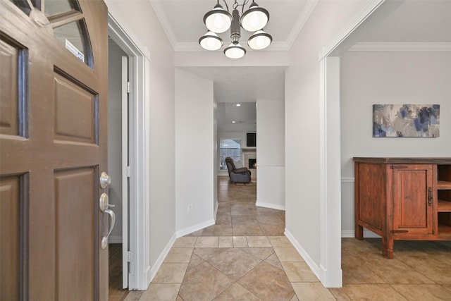 foyer entrance with light tile patterned floors, baseboards, a lit fireplace, crown molding, and a chandelier