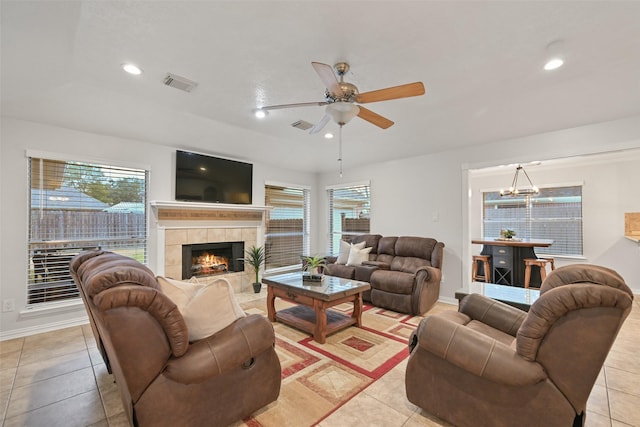 tiled living room featuring ceiling fan with notable chandelier and a fireplace