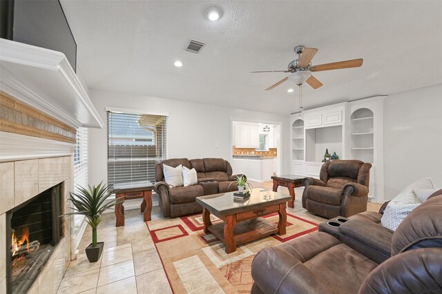 tiled living room with ceiling fan, a fireplace, and built in shelves